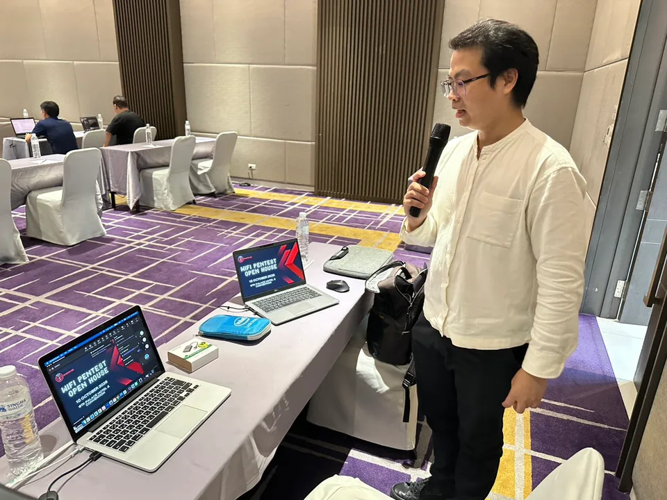 วิทยากรถือไมค์บรรยายใน WiFi Pentest Open House พร้อมคอมพิวเตอร์และผู้เข้าร่วมในห้อง
